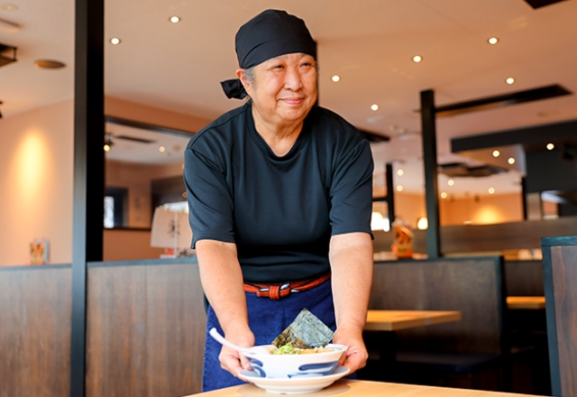 テーブルに料理を提供するシニアのT.H.さん