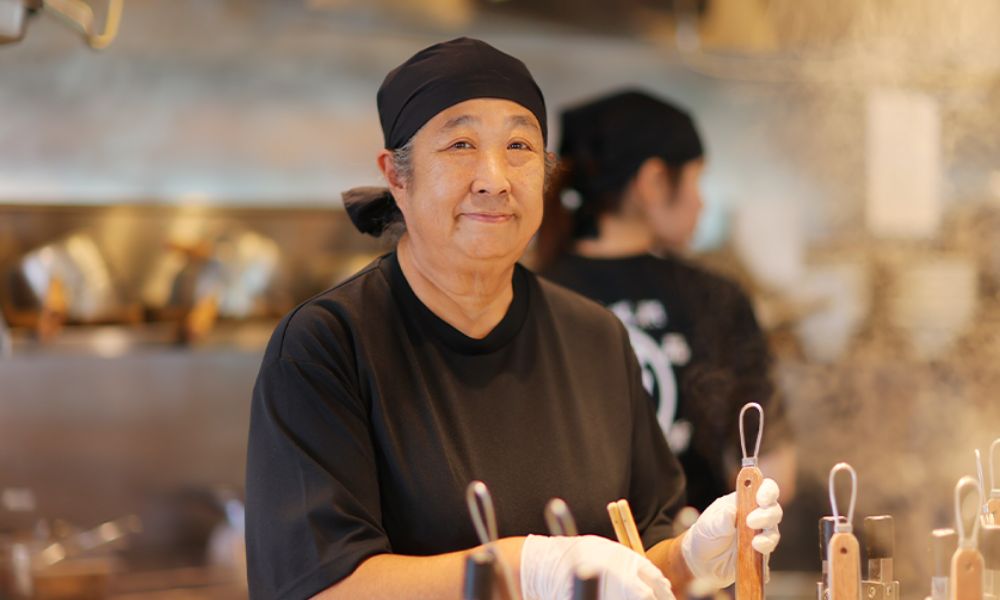 笑顔で料理を他のスタッフに手渡すシニア